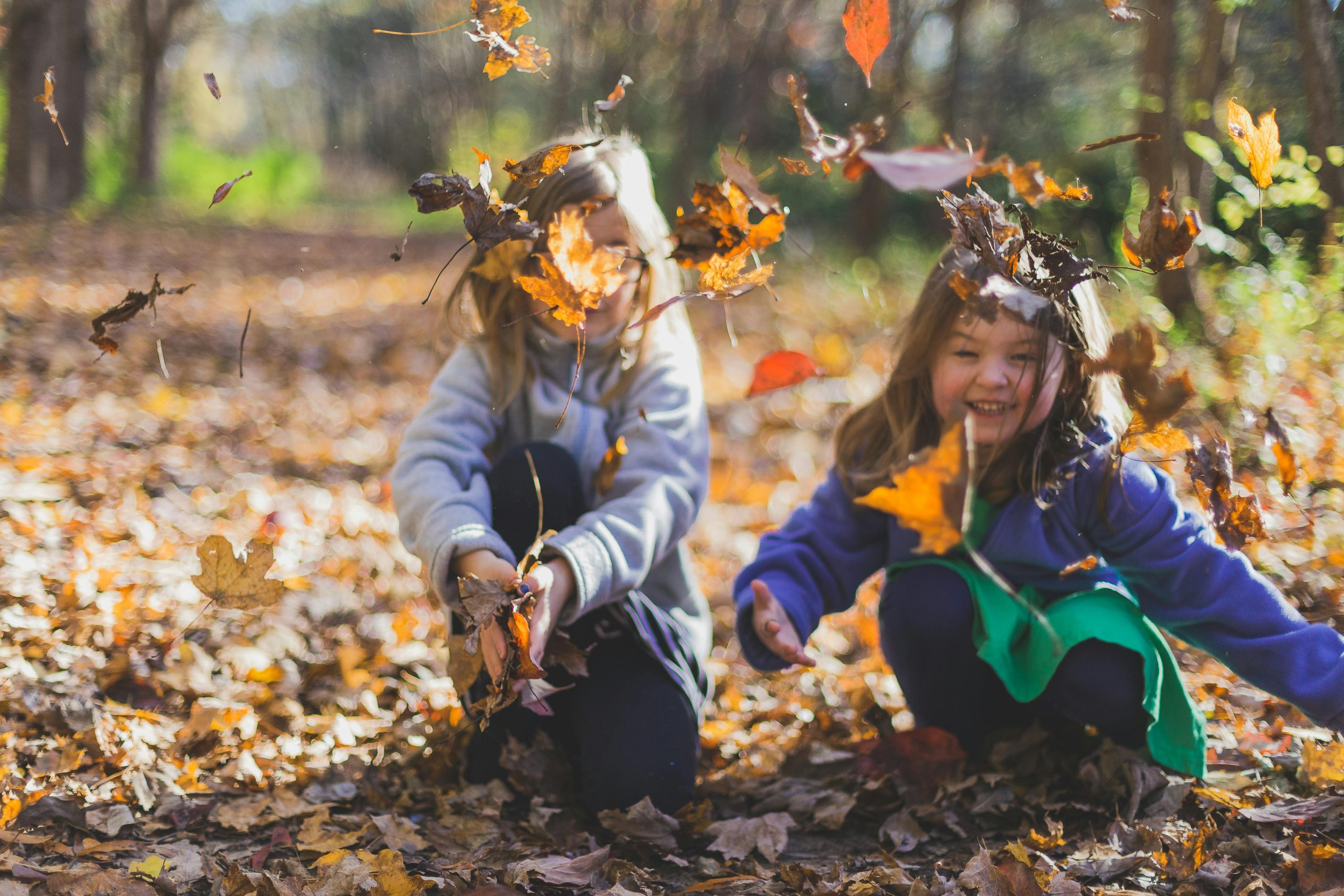 Dos niñas felices jugando y disfrutando del otoño con hojas secas